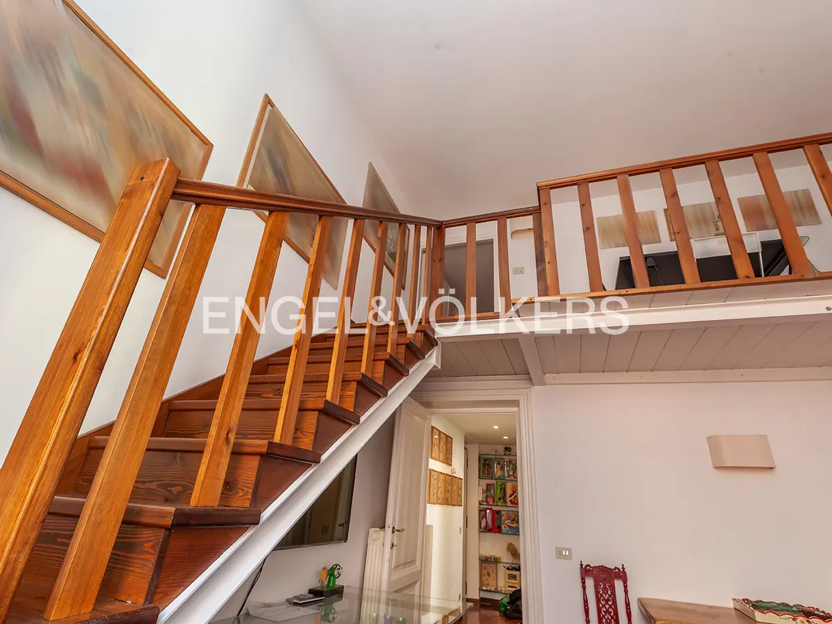 Interior view of a home featuring wooden stairs leading to a loft area with matching wooden railings. Artwork adorns the walls.