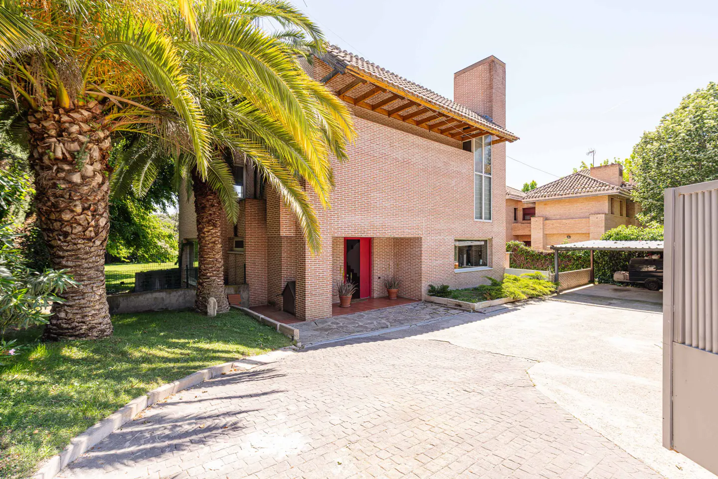 Exterior view of a two-story brick house with a red door, palm trees, and a paved driveway.