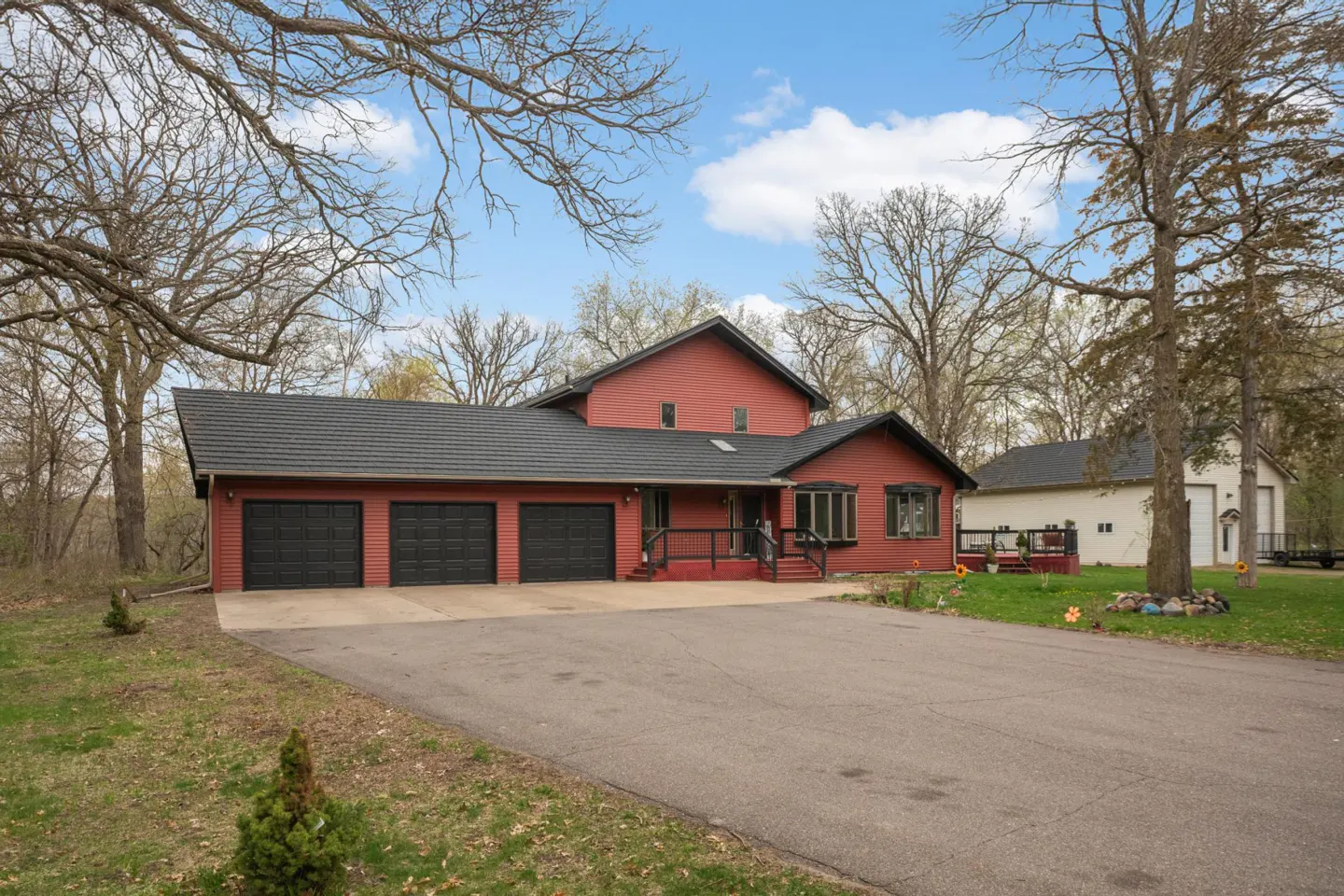 Red two-story house with a black roof and three-car garage. A long driveway leads up to the house.