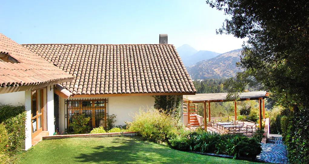 Exterior view of a white house with a terracotta tile roof, green lawn, and patio with mountain views.
