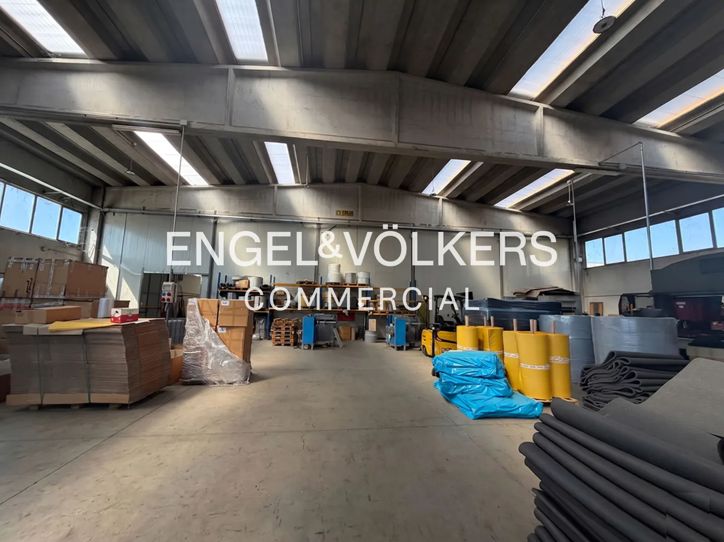 A wide shot of a large warehouse with boxes, equipment, and the Engel & Völkers Commercial logo.