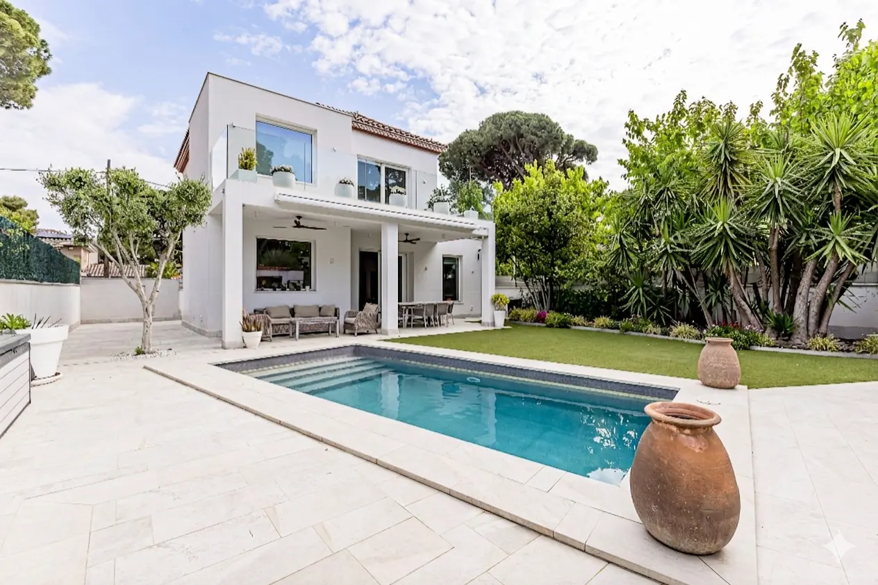 A modern white house with a blue swimming pool, patio furniture, and green lawn.