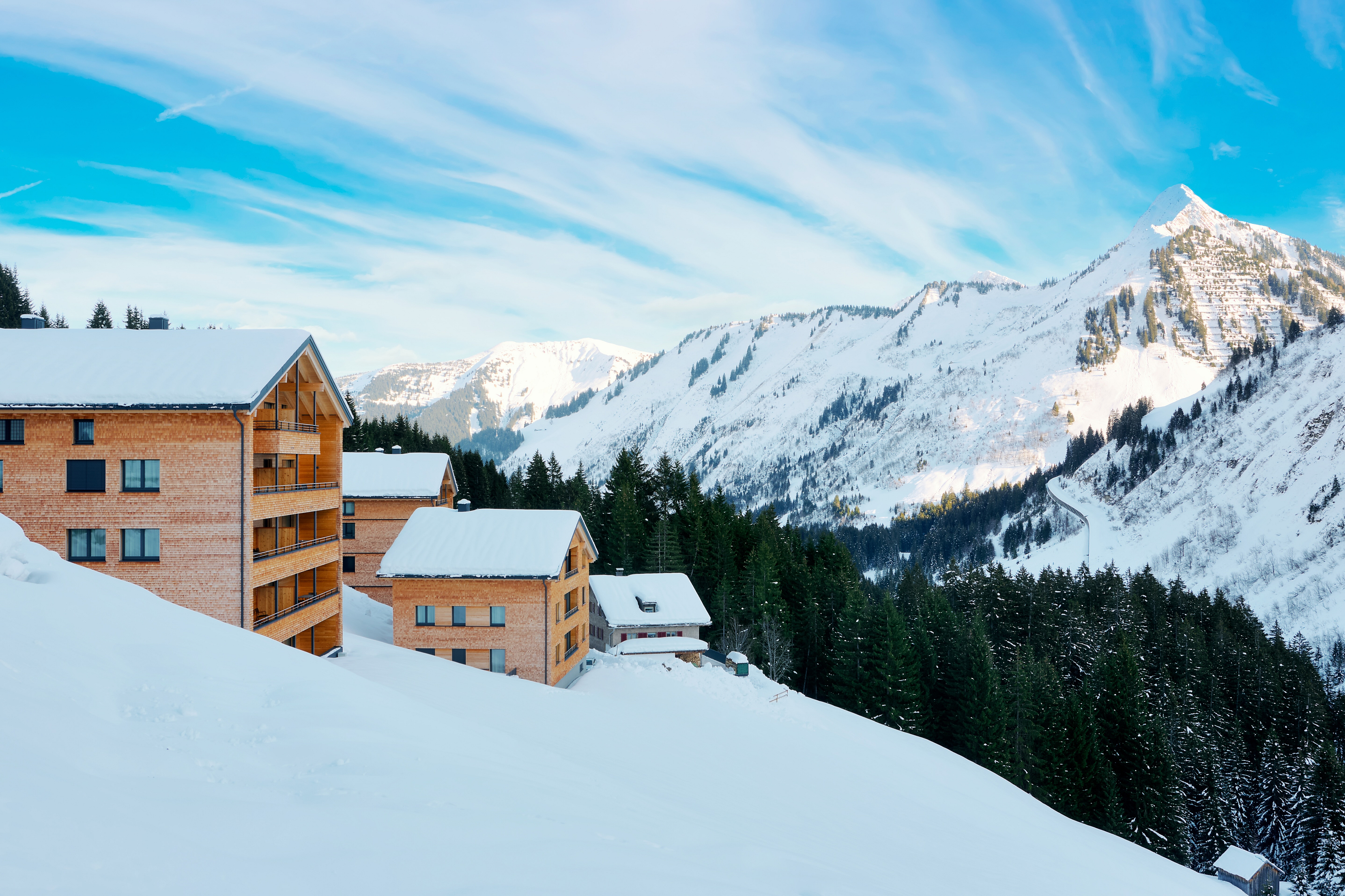 Modern wooden chalets nestled in a snowy mountain landscape under a bright blue sky with wispy clouds. [AI-generated text]