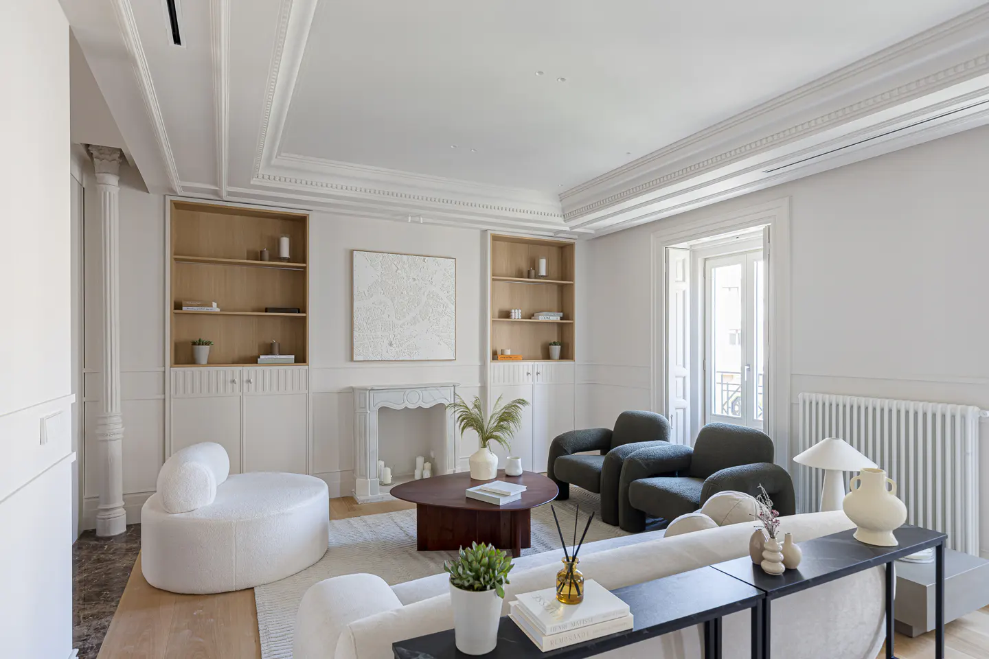 Bright living room with white walls, crown molding, built-in shelves, fireplace, and modern furniture including gray chairs and a white sofa.