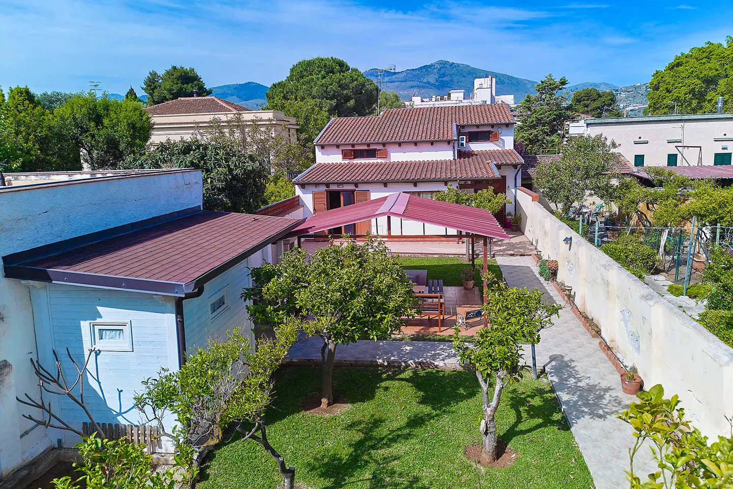 Aerial view of a white house with a red tile roof, a green lawn, and a patio with a red awning.