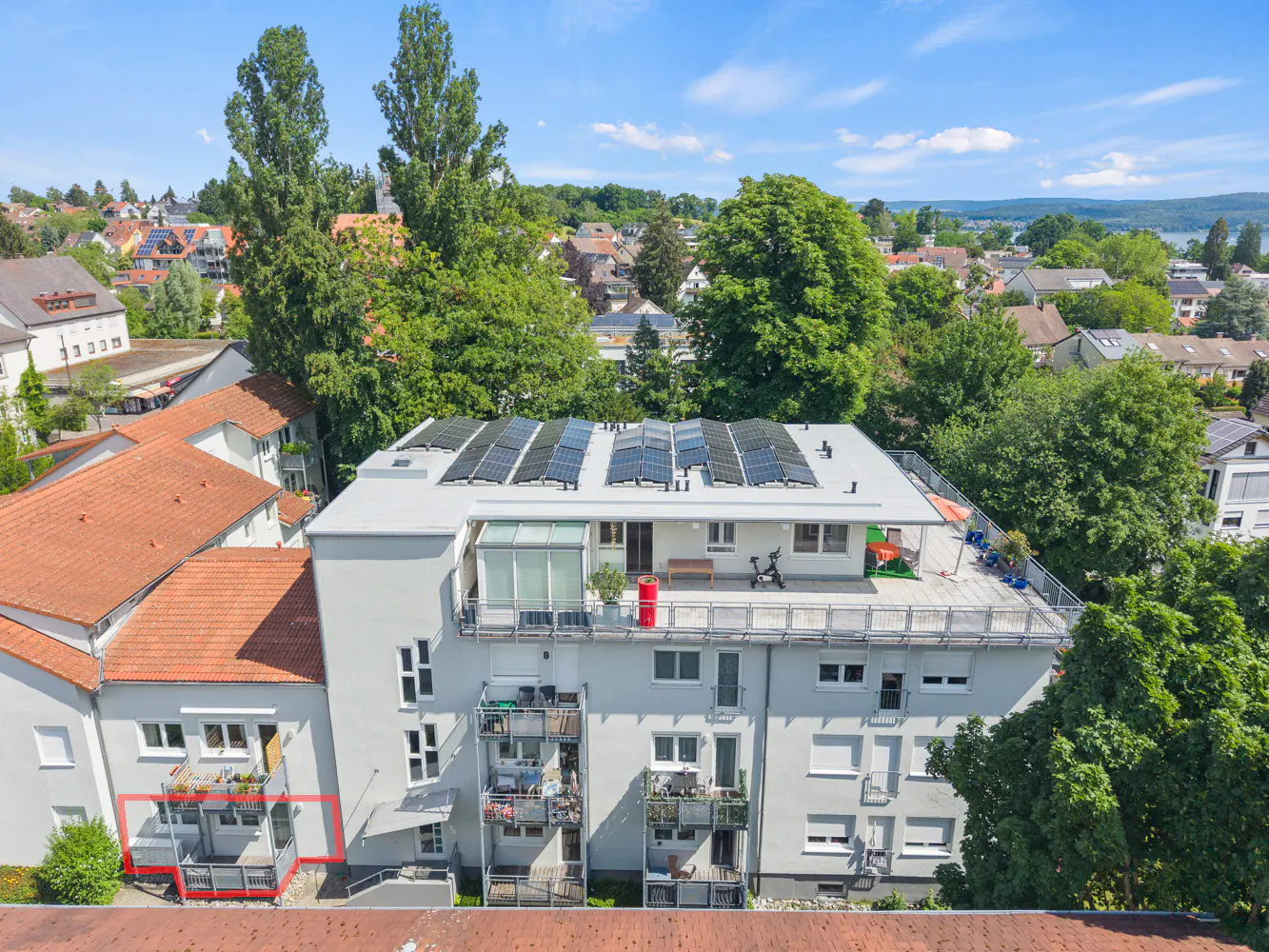 Aerial view of a multi-story apartment building with solar panels on the roof and a highlighted balcony on the left.