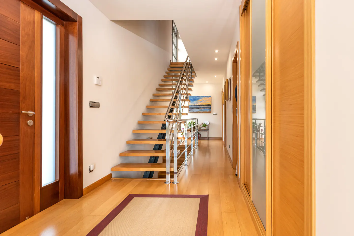Hallway with wood floors, a staircase with metal railings, and a wood door with a glass panel.