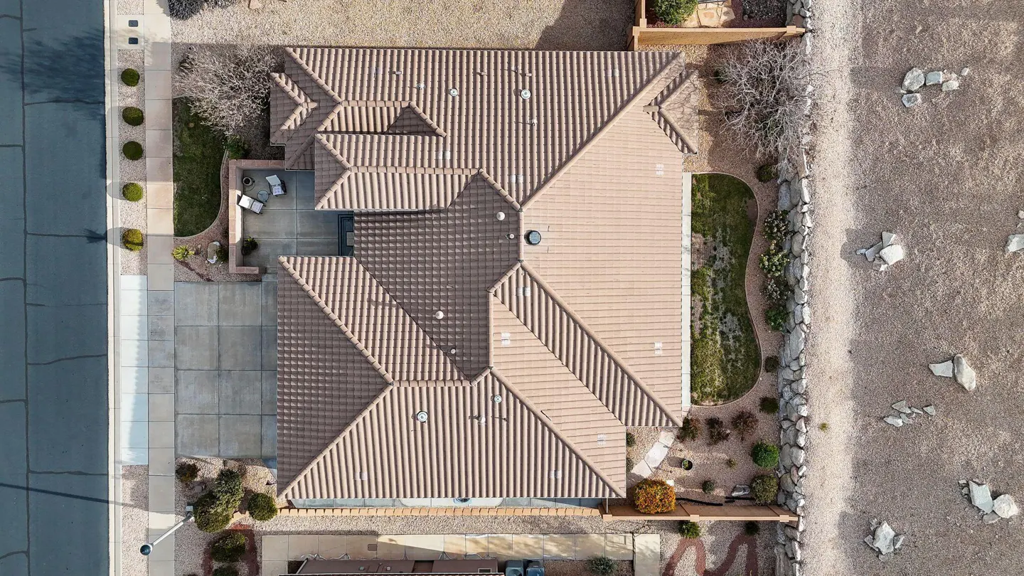 Aerial view of a single-story house with a brown tile roof, a concrete driveway, and a small backyard with green grass.