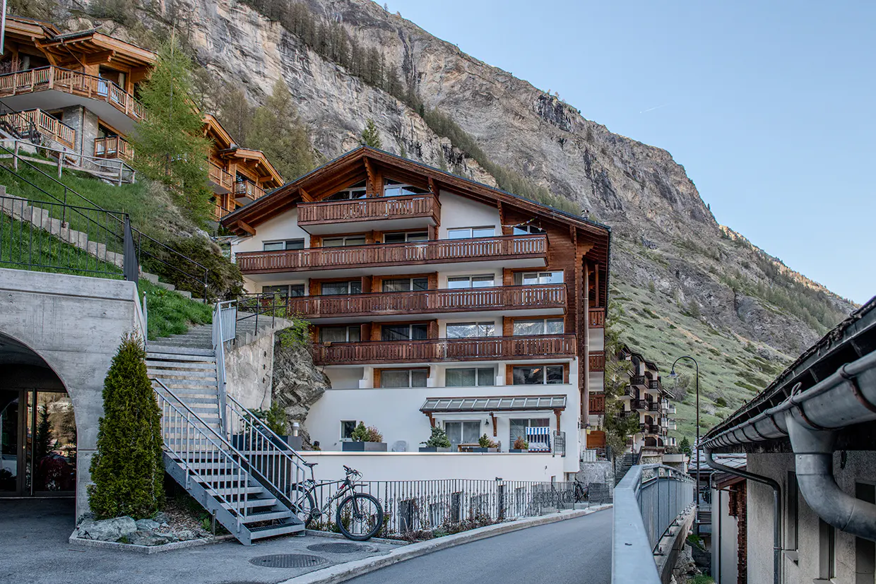 A multi-story chalet with wood balconies sits on a hillside, with a bike parked nearby.