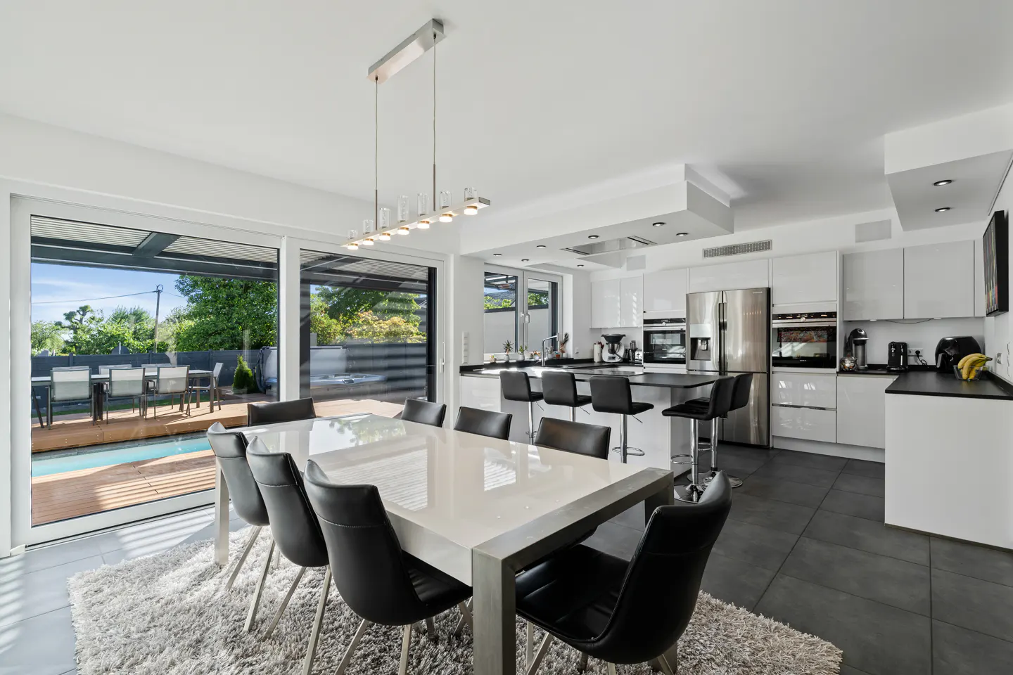 Bright, modern kitchen and dining area with white cabinets, black chairs, and a view of the pool.