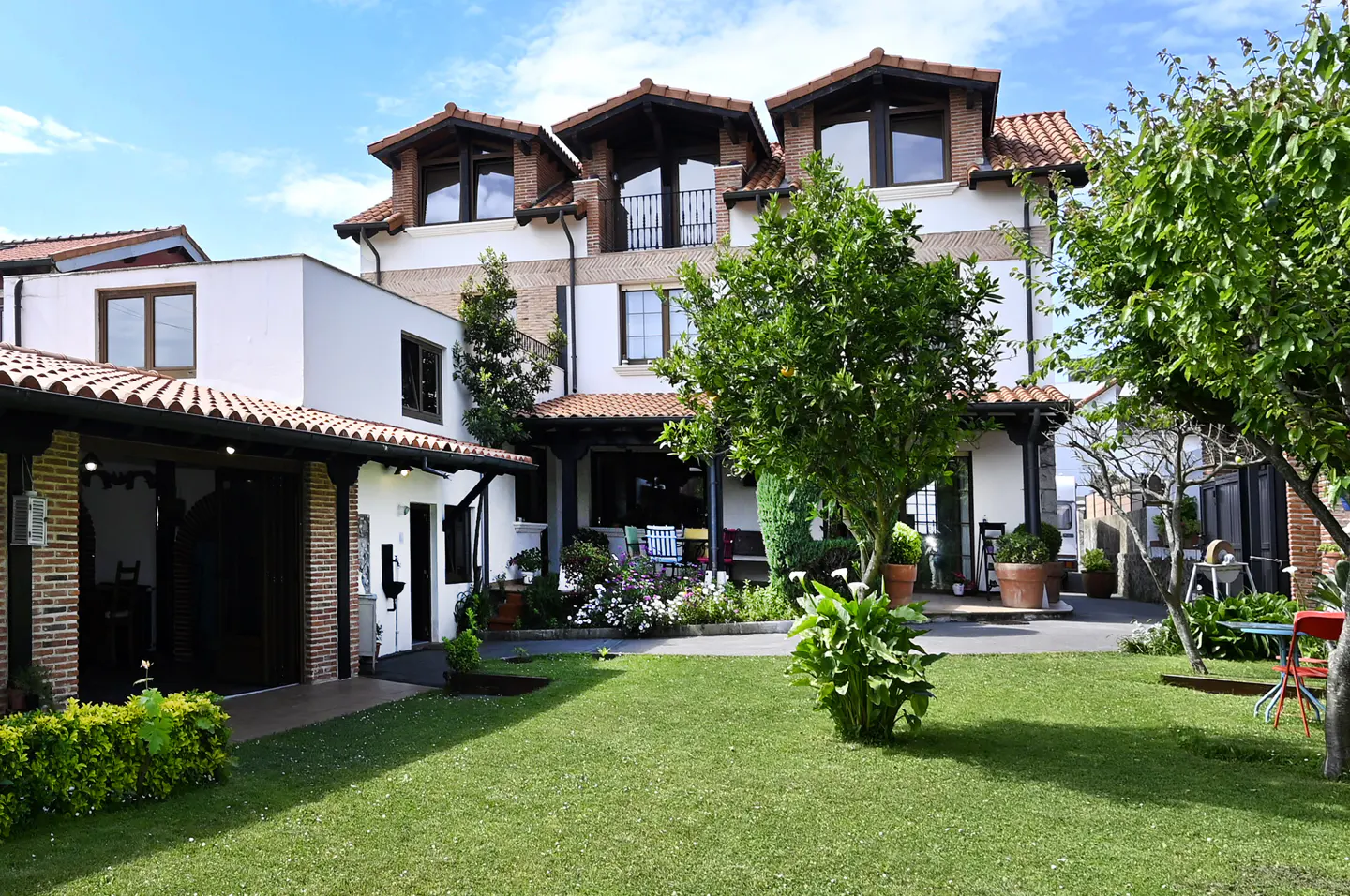 Exterior view of a white house with a red tile roof and green lawn under a blue sky.