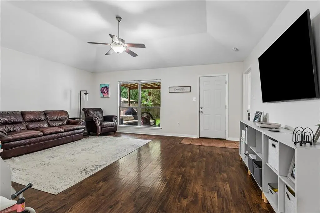 Living room with dark wood floors, brown leather sofa and chair, ceiling fan, and large window to backyard.