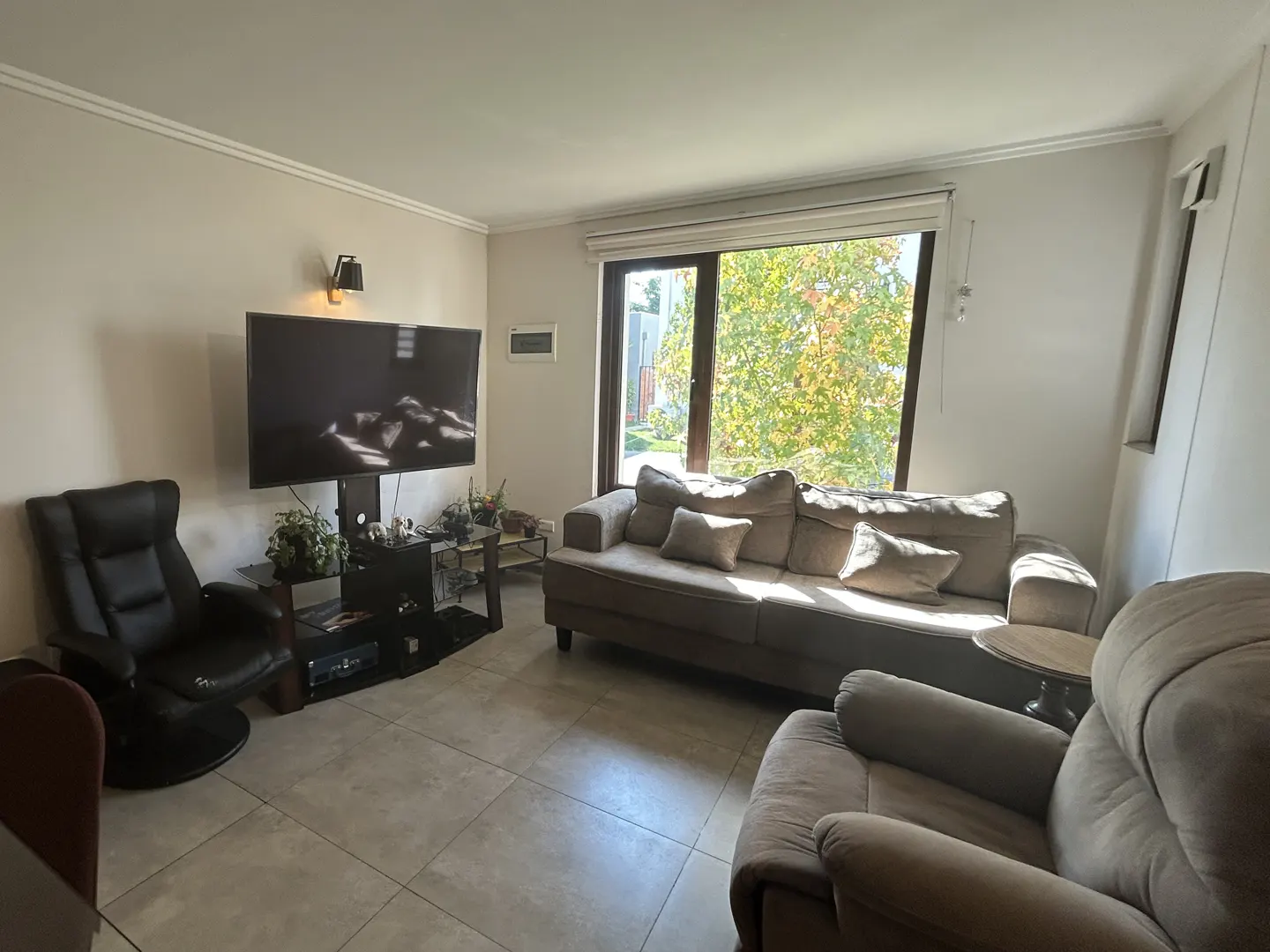 Living room with a large window, a gray sofa, a black recliner, and a TV on a stand.