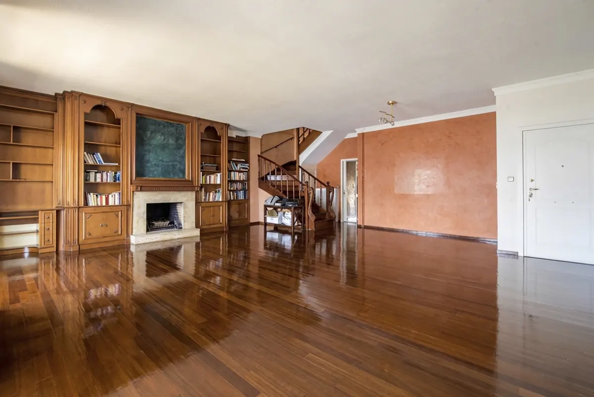 Spacious living room with hardwood floors, a fireplace, built-in bookshelves, and a spiral staircase. The walls are orange and white.
