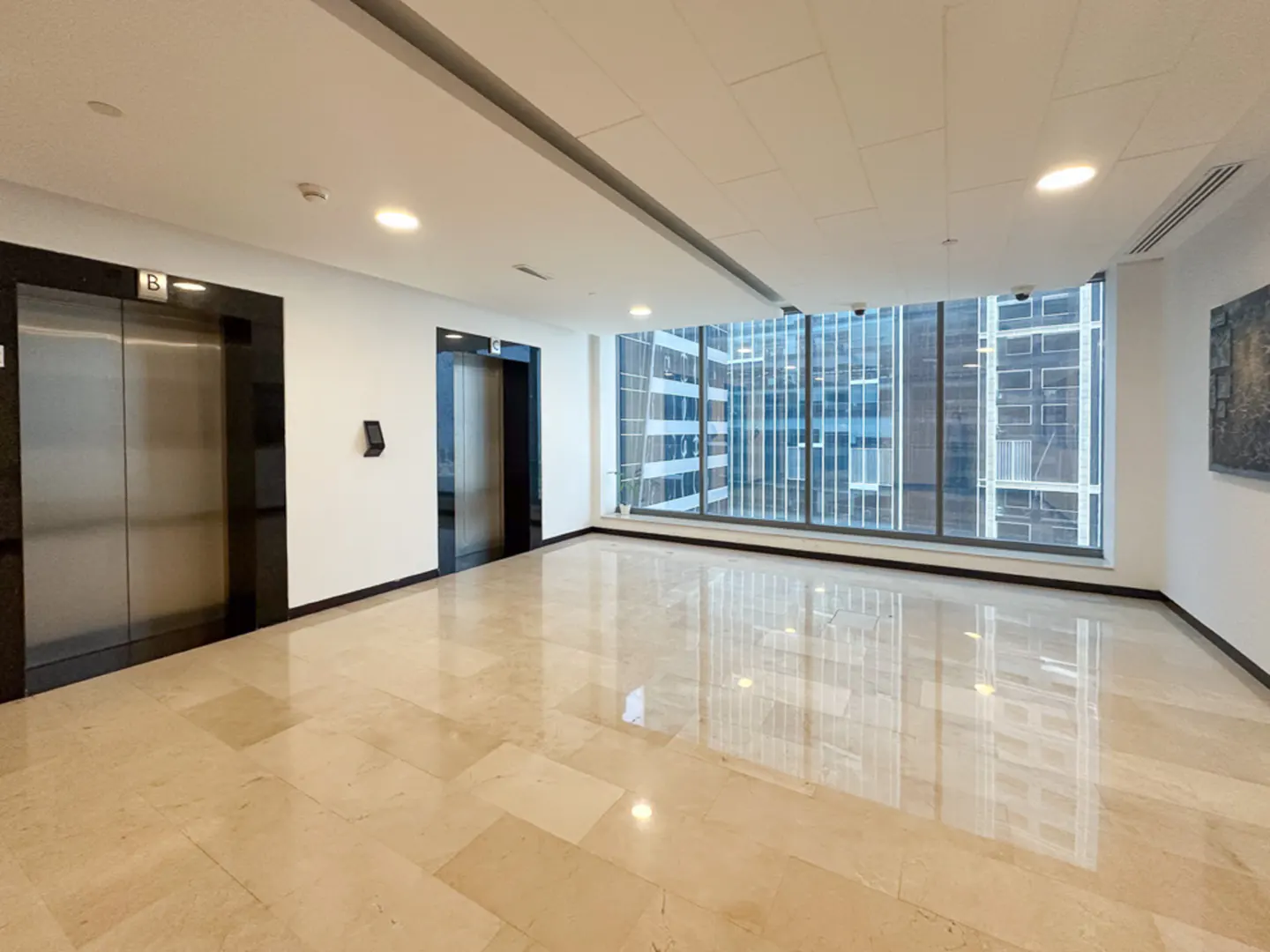 Office lobby with marble floors, two elevators, and a large window with a city view.