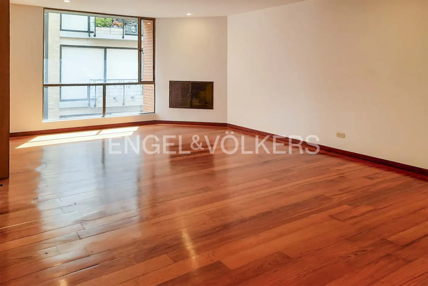 Empty room with hardwood floors, white walls, and a large window. Engel & Völkers logo is visible.