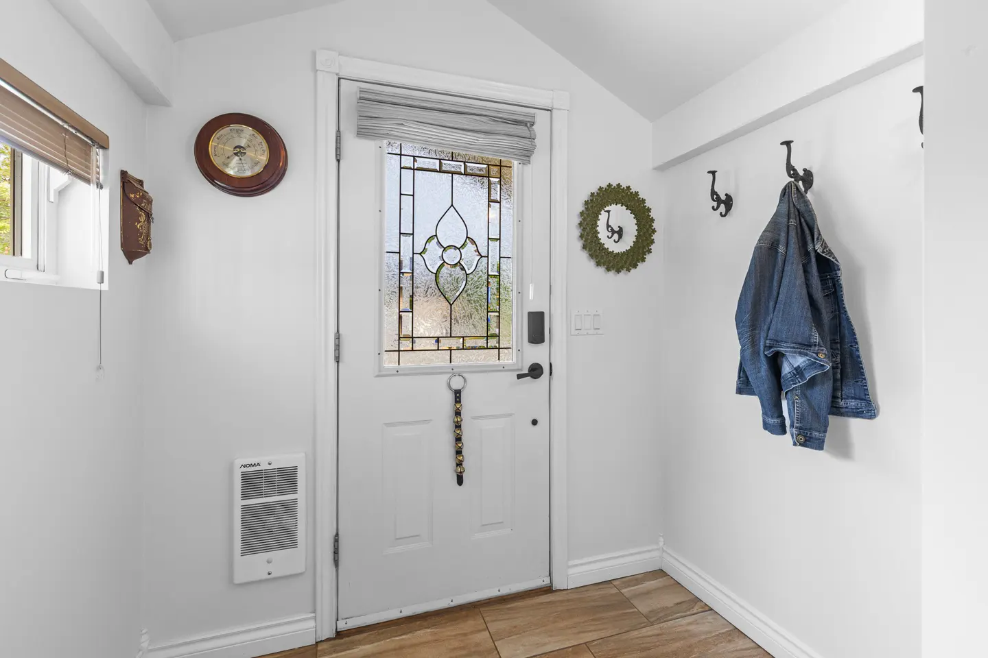 Entryway with a white door with a decorative glass window, a denim jacket hanging on a hook, and a wooden clock on the wall.