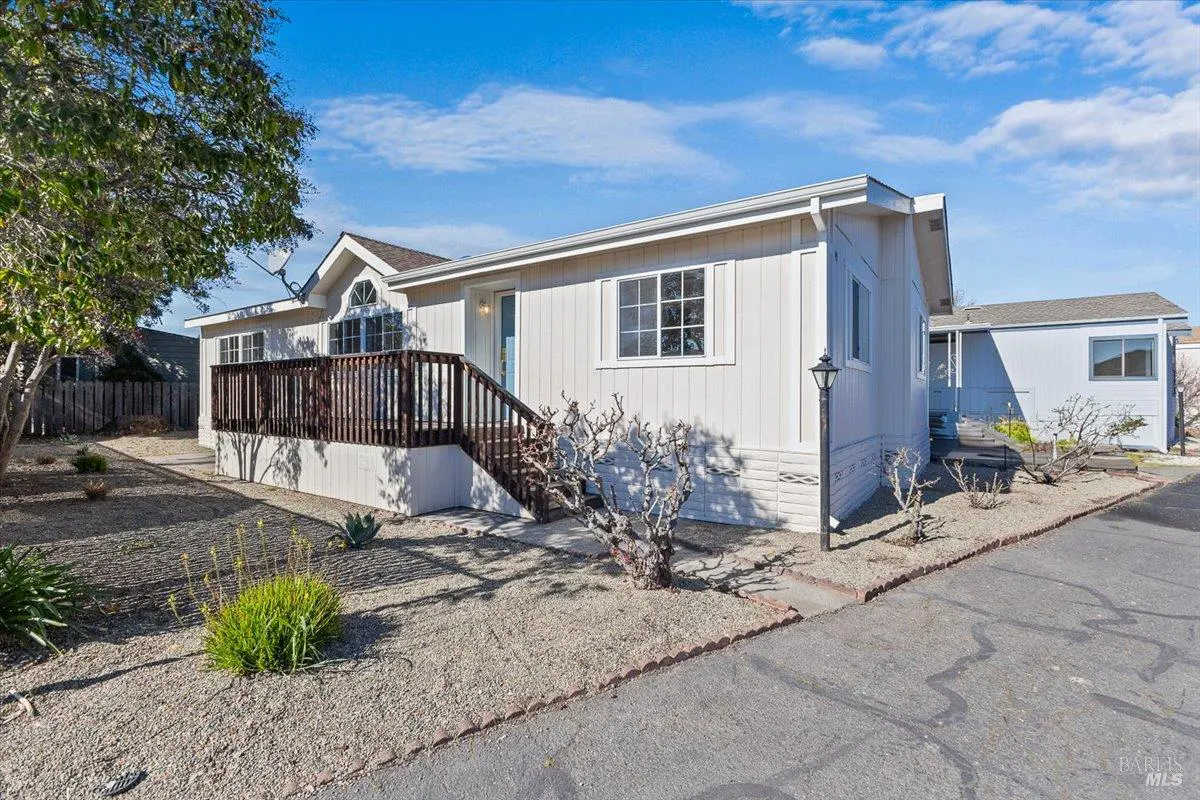 Exterior of a white single-story home with a brown deck and stairs, under a blue sky.