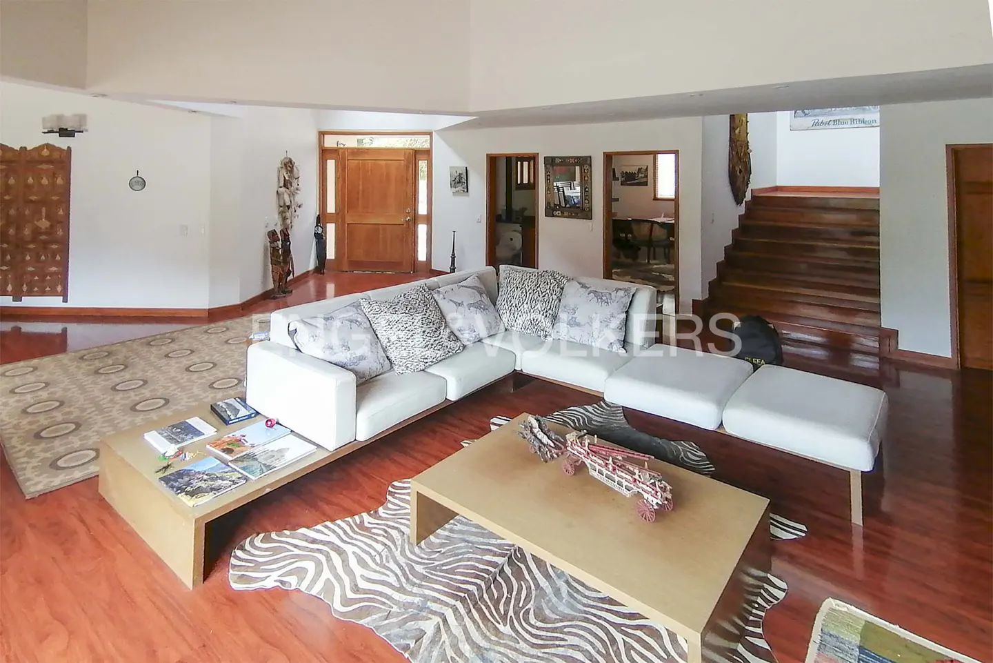 Bright living room with white sectional sofa, zebra rug, and wood floors. Stairs and front door visible.