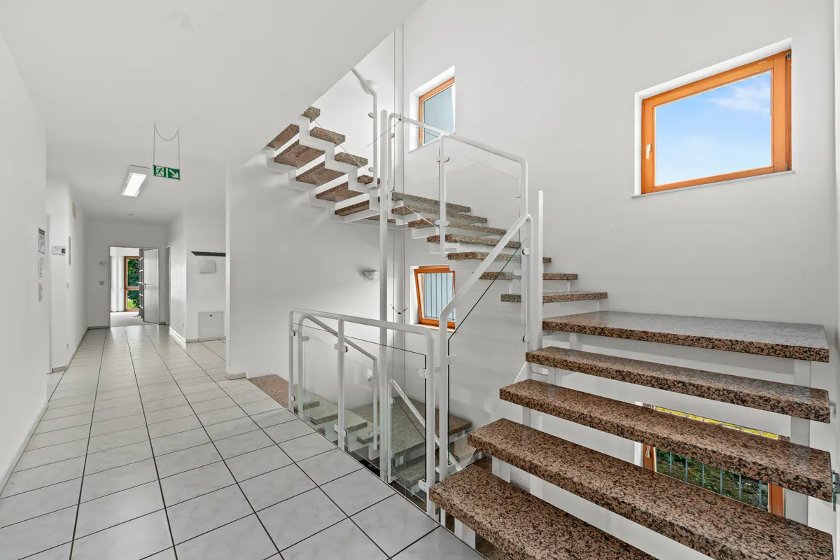 Modern interior with white walls, tiled floor, and a floating staircase featuring granite steps and glass railings.