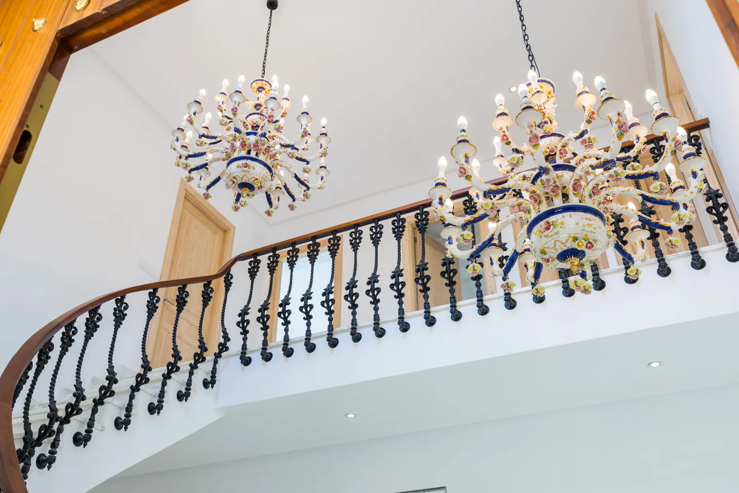 Interior view of a staircase with ornate black railings, two decorative chandeliers, and white walls.