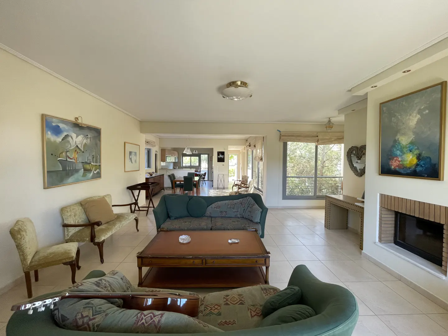 Bright, open living room with green sofas, a wooden coffee table, and paintings on the walls. A guitar rests on a sofa.