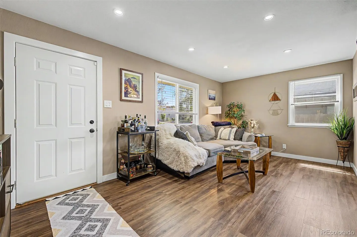 Living room with wood floors, a gray sectional sofa, a bar cart, and a white front door.