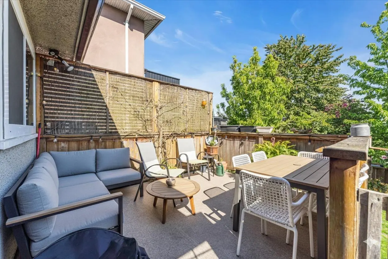 Outdoor patio with gray sectional, table, and chairs. A wooden fence and green trees provide privacy.