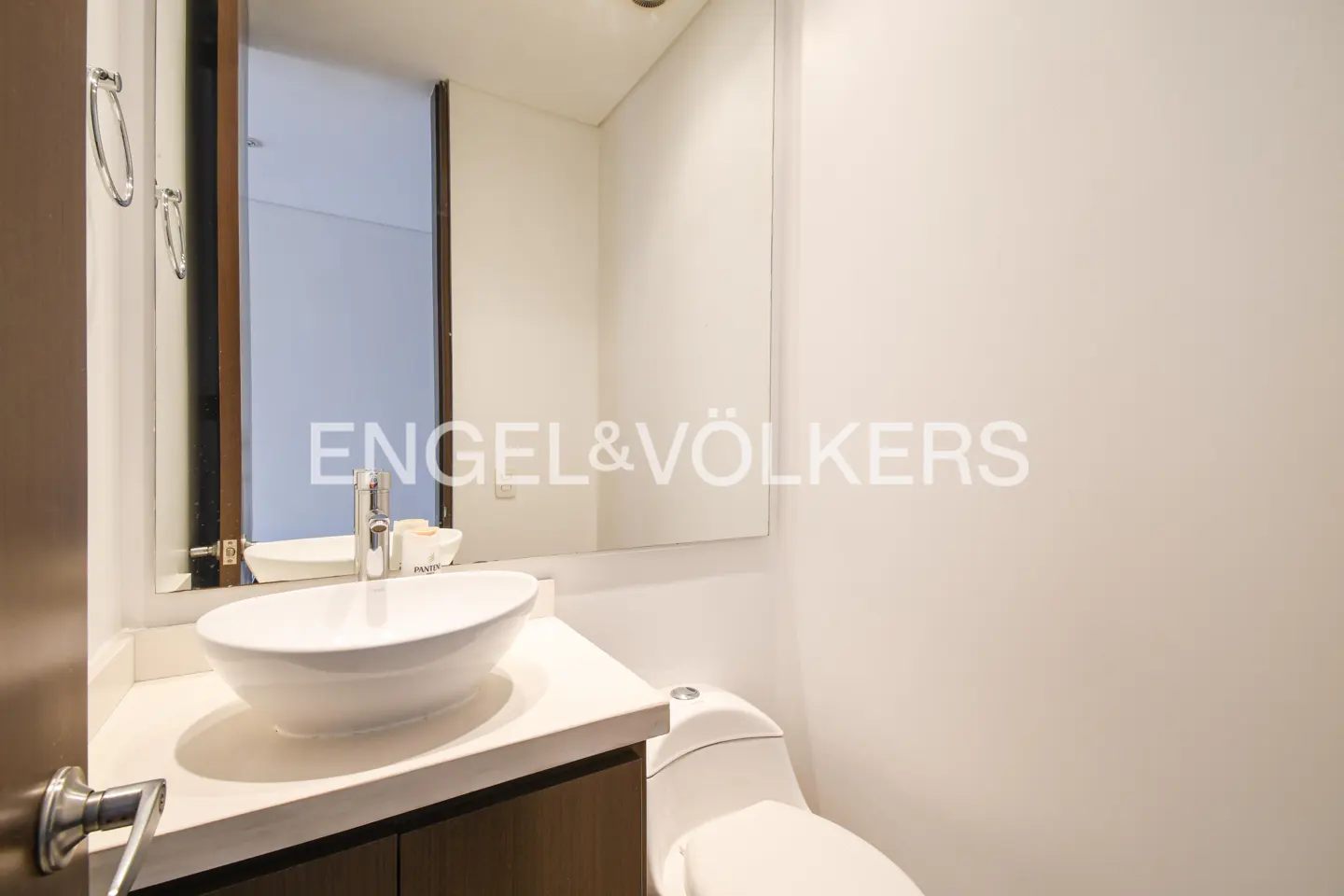 A modern bathroom features a white sink, toilet, and walls, with a large mirror above the sink.