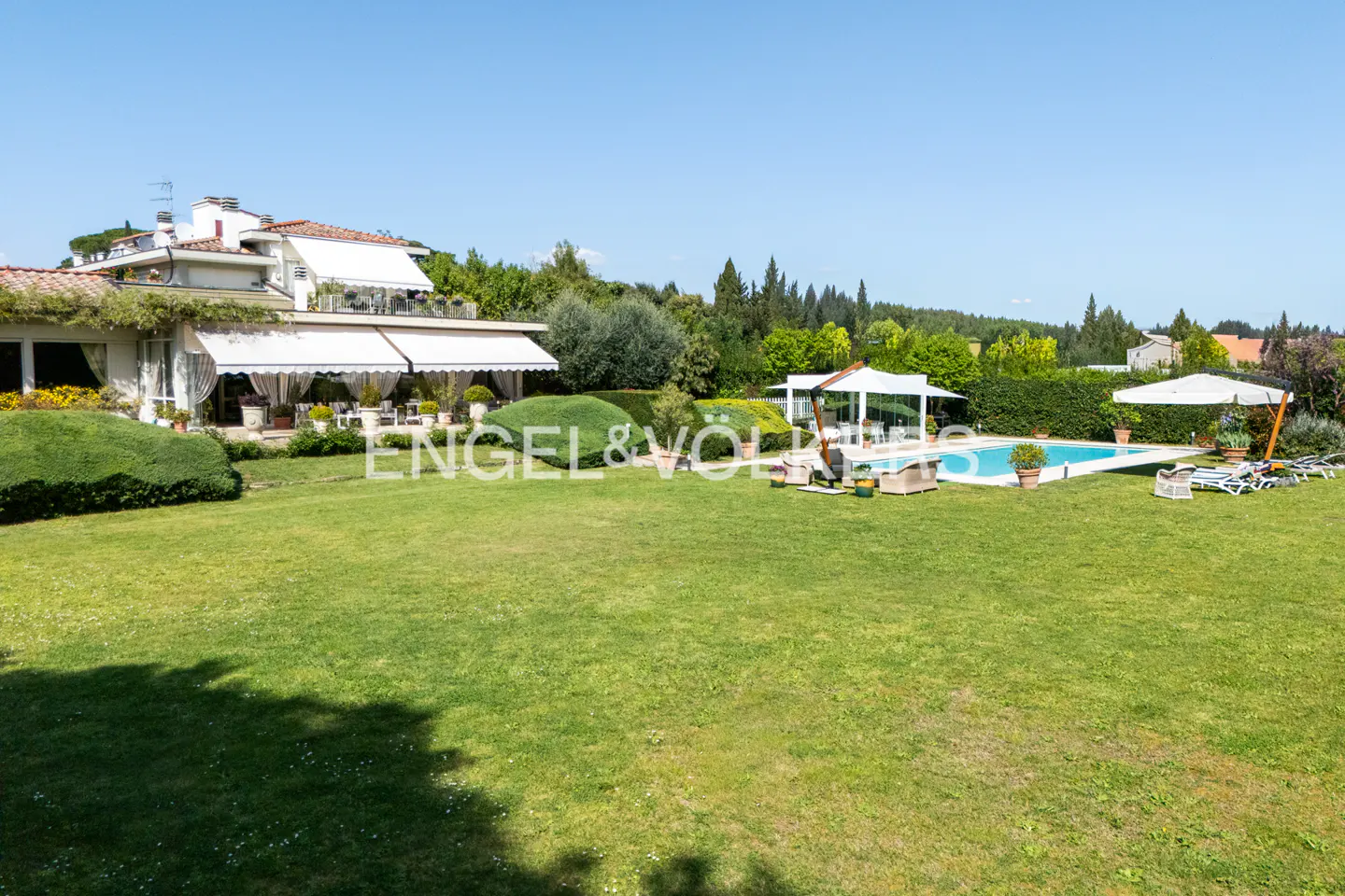 A wide shot of a house with a large green lawn, pool, and patio furniture.
