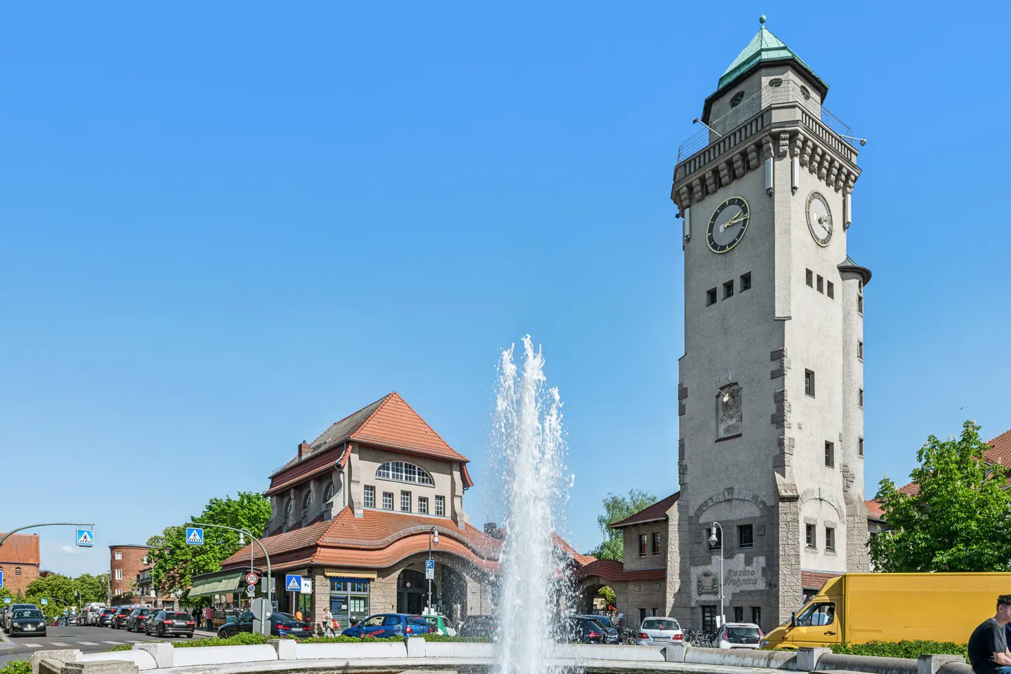 Cityscape view of Steglitz Town Hall clock tower and fountain under a clear blue sky.