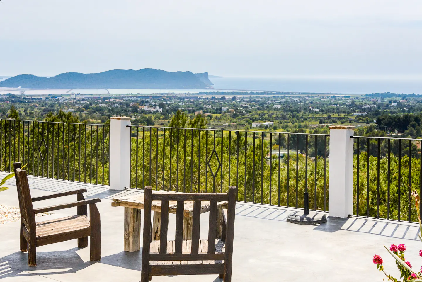 Outdoor patio with two wooden chairs and a table overlooking a green landscape and ocean view.