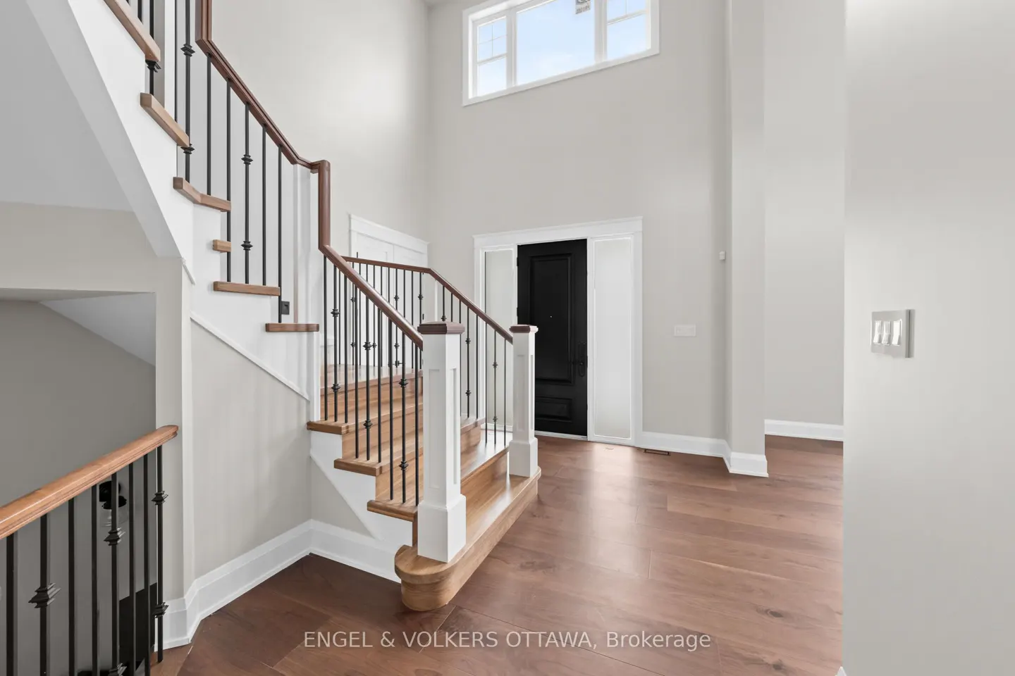 Interior view of a home foyer with hardwood floors, a staircase with wood and black iron railings, and a black front door.
