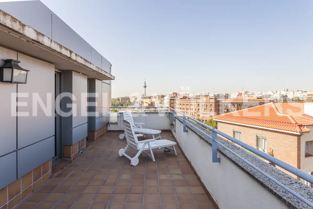 Balcony view with two white chairs, brown tiled floor, and city skyline in the background.
