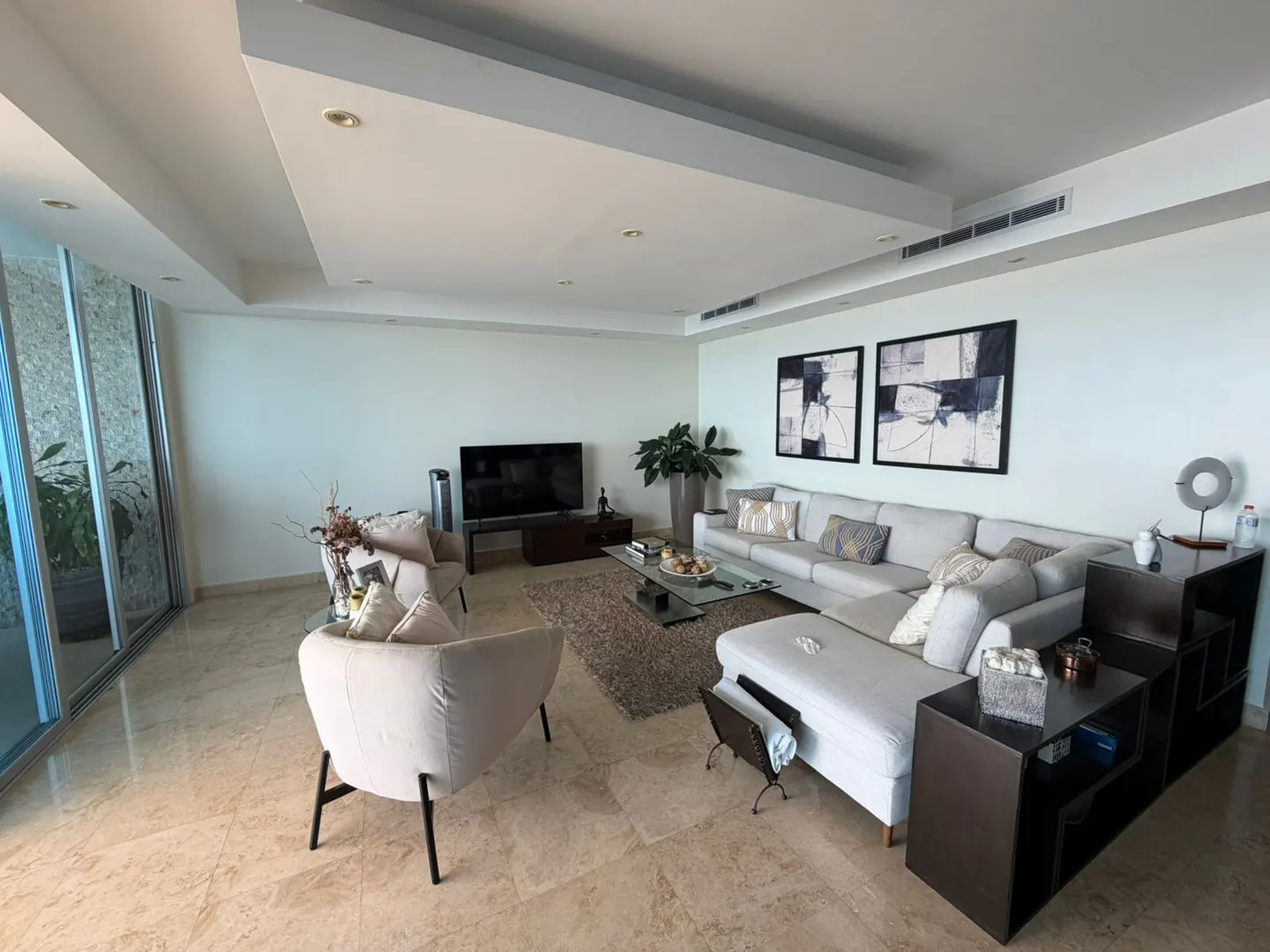 Modern living room with beige tile floors, a large white sectional sofa, two armchairs, and a glass coffee table.