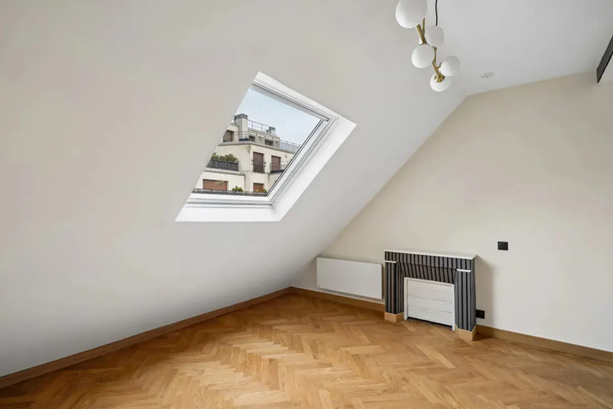 Attic room with herringbone wood floors, white slanted walls, a skylight, and a decorative striped fireplace mantel.