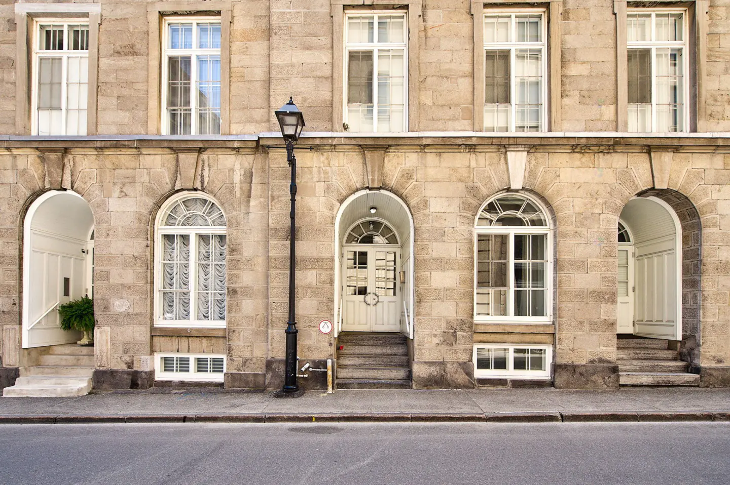 Exterior of a stone building with arched doorways, white windows, and a black lamppost.