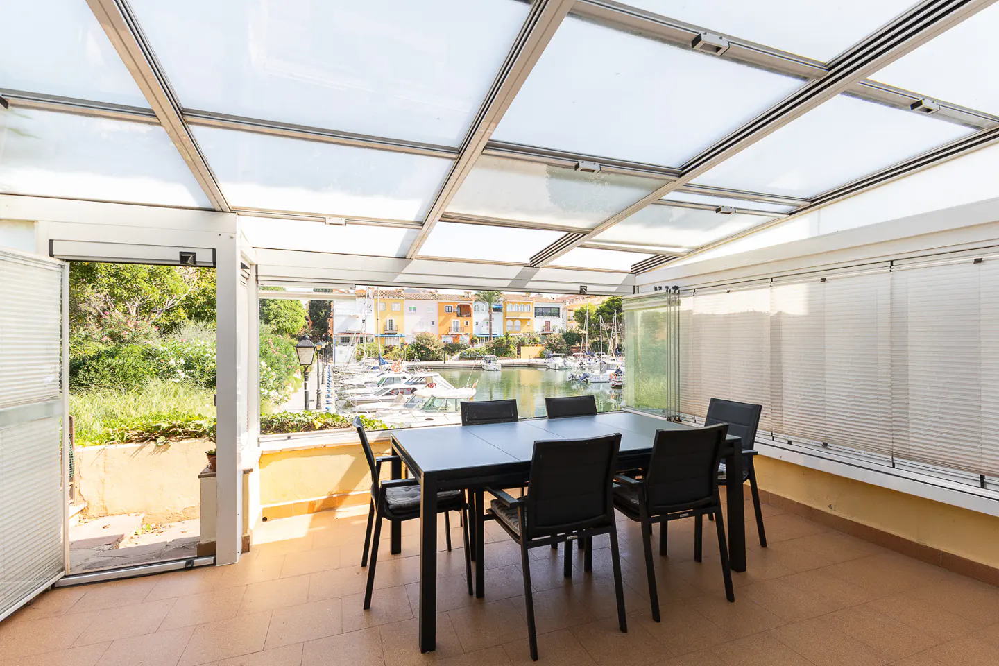 Enclosed patio with a black table and six chairs. A marina is visible through the glass walls.