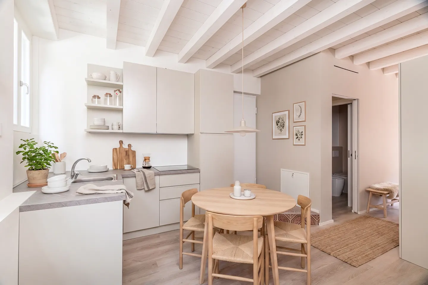 Modern kitchen with beige cabinets, a round wooden dining table, and white exposed ceiling beams.