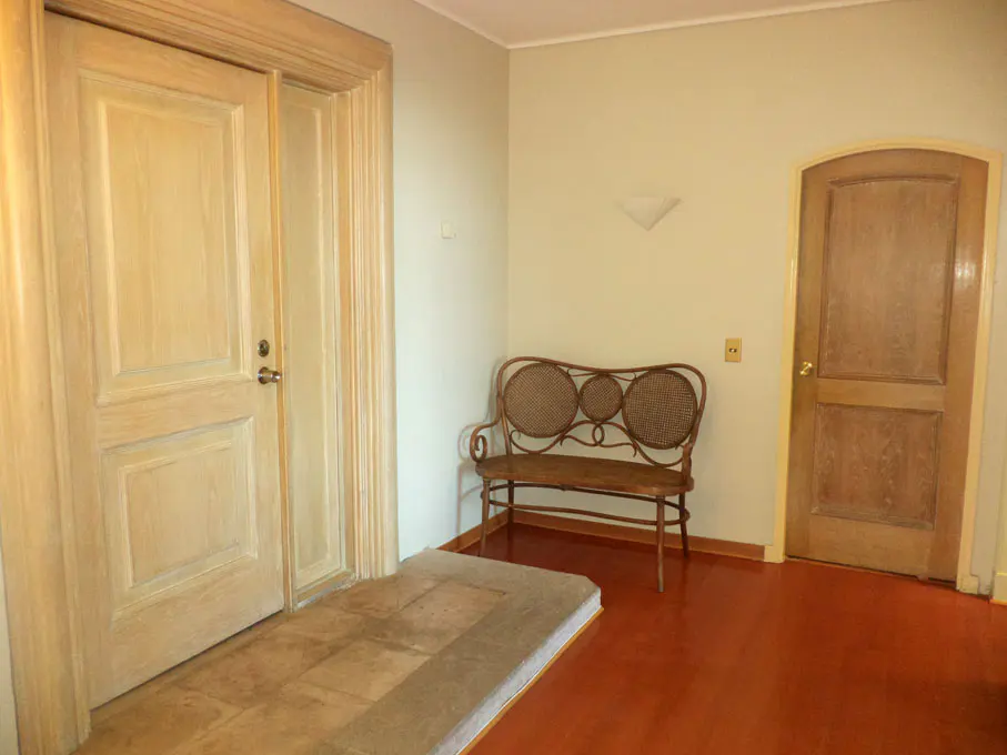 Hallway with a light wood door, a wicker bench, and a brown door on a red wood floor.