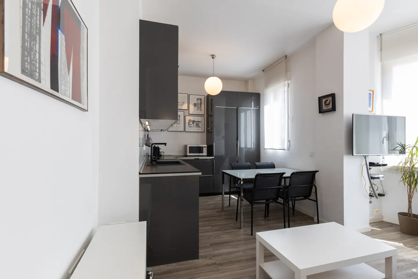 A modern apartment interior with gray cabinets, a dining table, and a white coffee table. A TV is mounted on the wall.