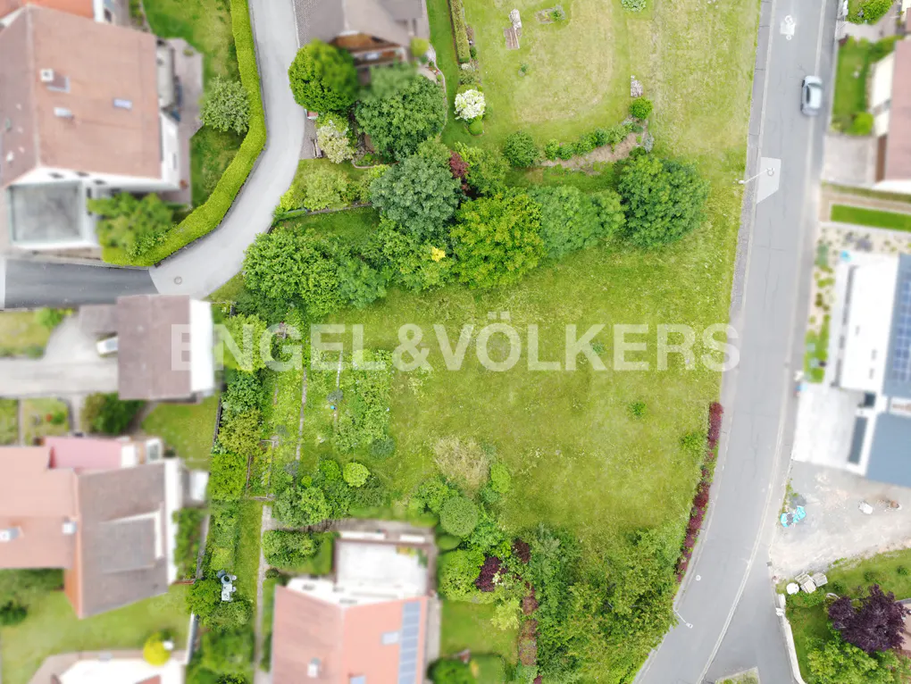 Aerial view of a grassy lot for sale, surrounded by houses and trees, with the Engel & Völkers logo overlaid.