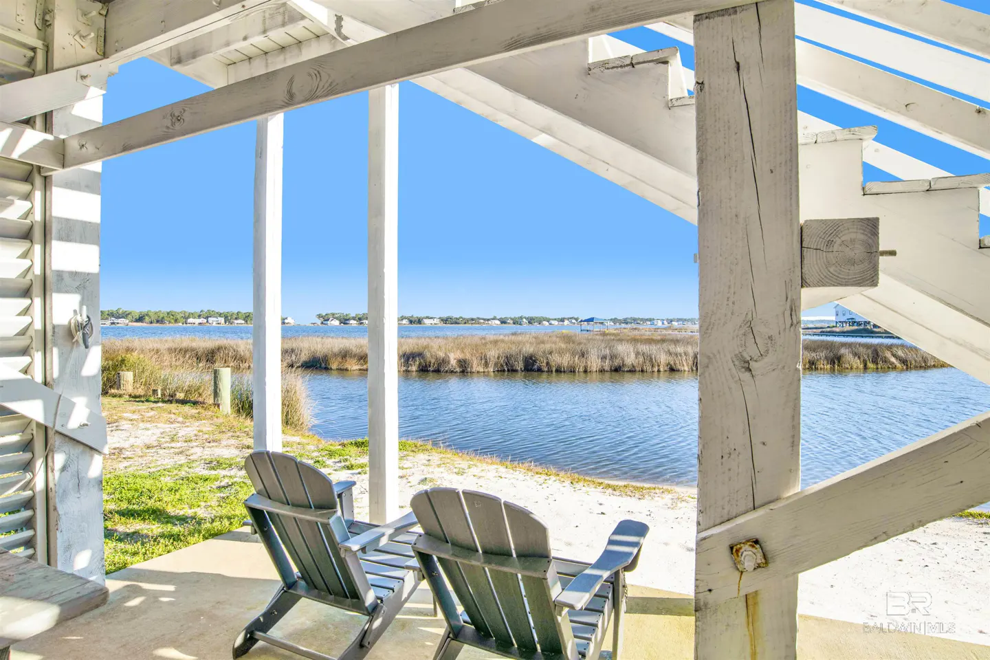 View from a white porch with two Adirondack chairs overlooking a blue bay on a sunny day.
