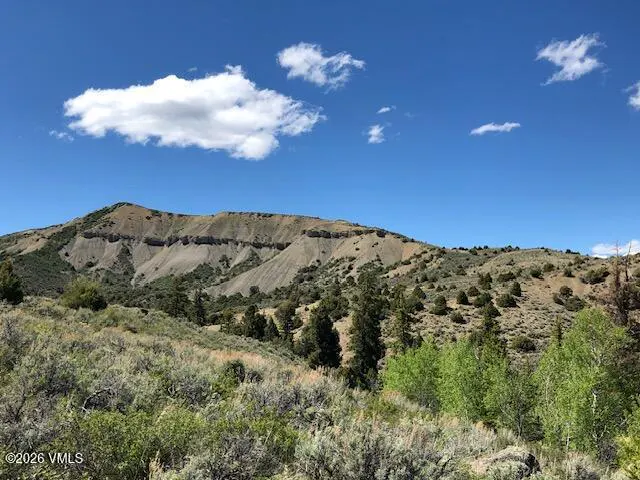 Landscape view of a mountain range with sparse trees under a blue sky with scattered white clouds.