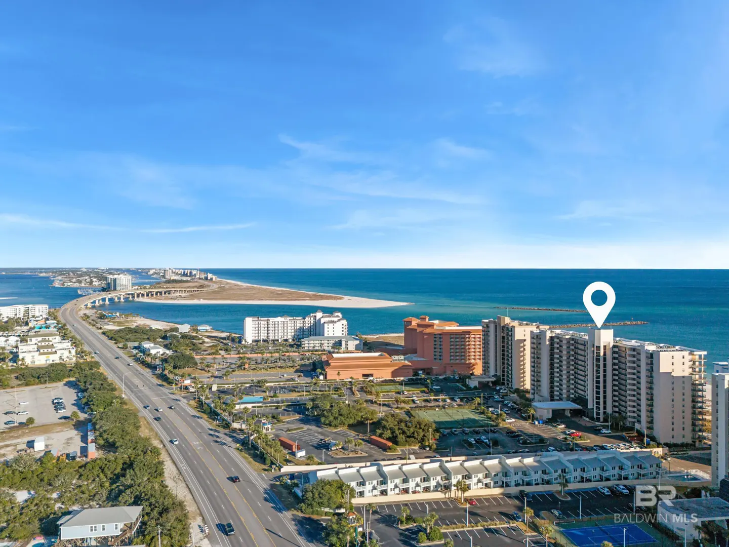Aerial view of a beachfront property with a white location pin on top of a high-rise building. Blue sky and ocean in the background.