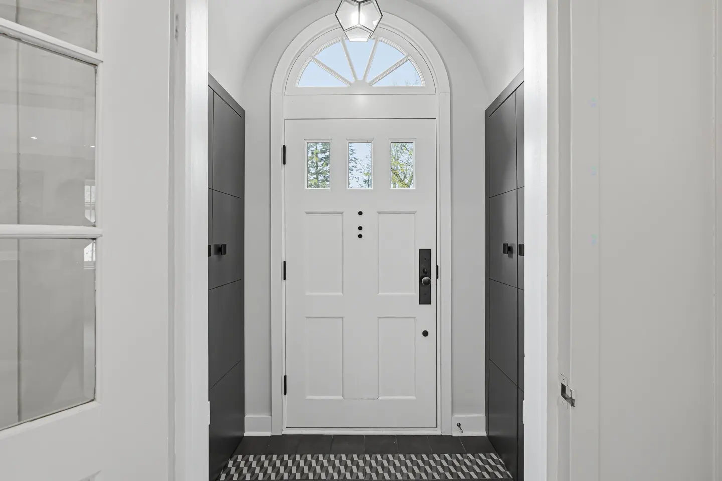 A white front door with glass panes and an arched transom window, flanked by gray cabinets in a white entryway.