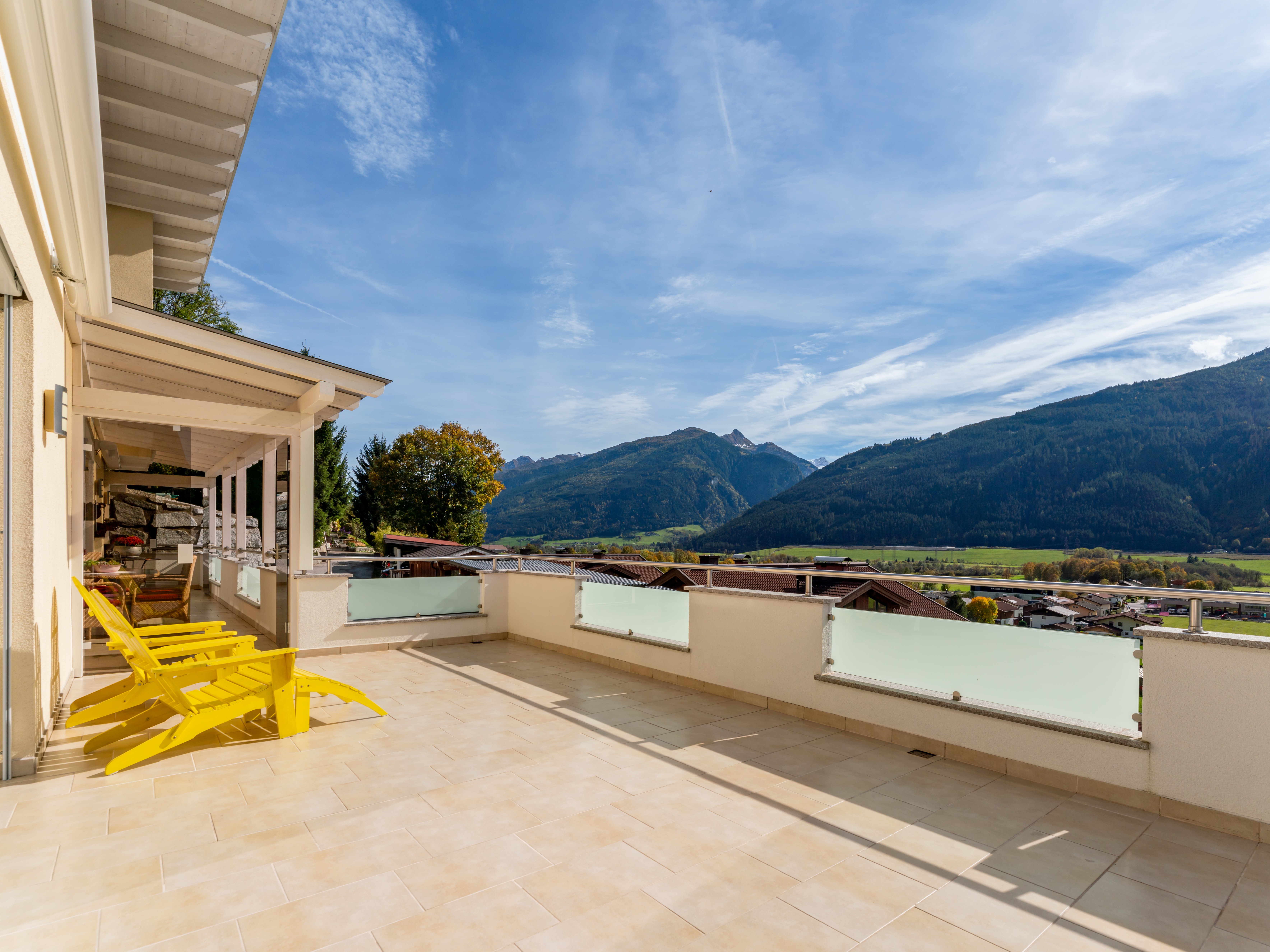 Spacious balcony with yellow lounge chairs overlooking a scenic valley and mountain range under a bright blue sky.