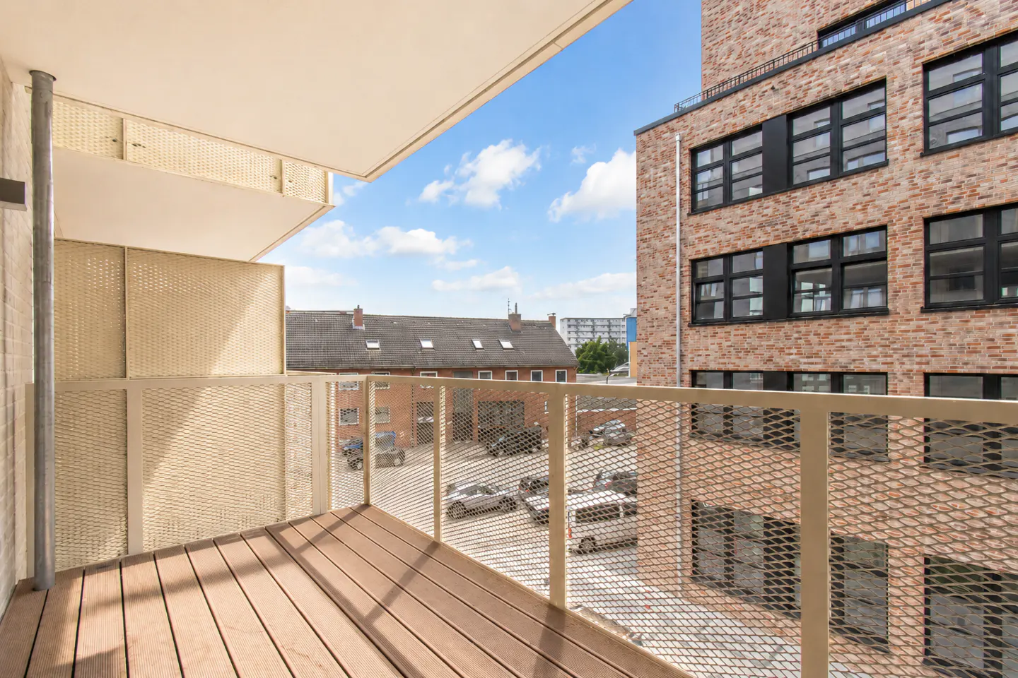 View from a modern balcony with wooden flooring and metal railings overlooking a brick building and a parking lot.