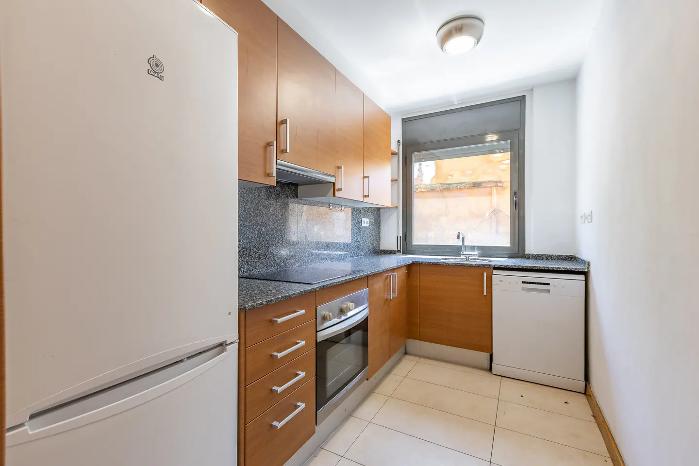 A bright kitchen with wood cabinets, granite countertops, and white appliances. A window provides natural light.