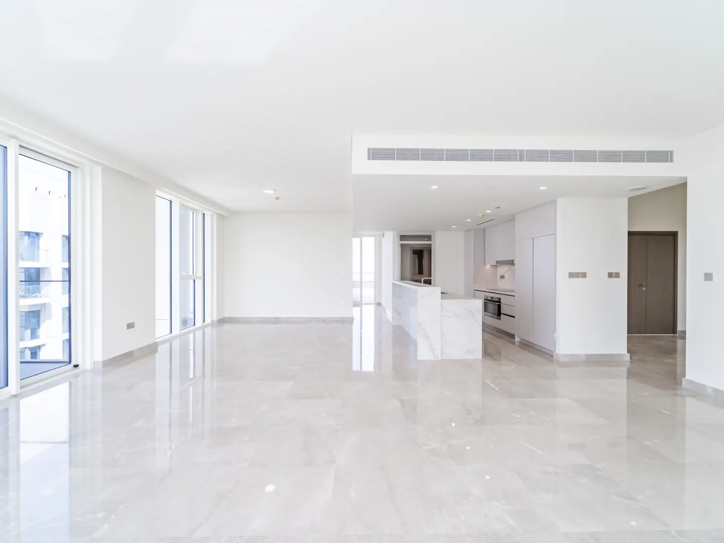 Spacious, bright open-plan living area with white walls, glossy marble floors, and a modern kitchen with a marble island.